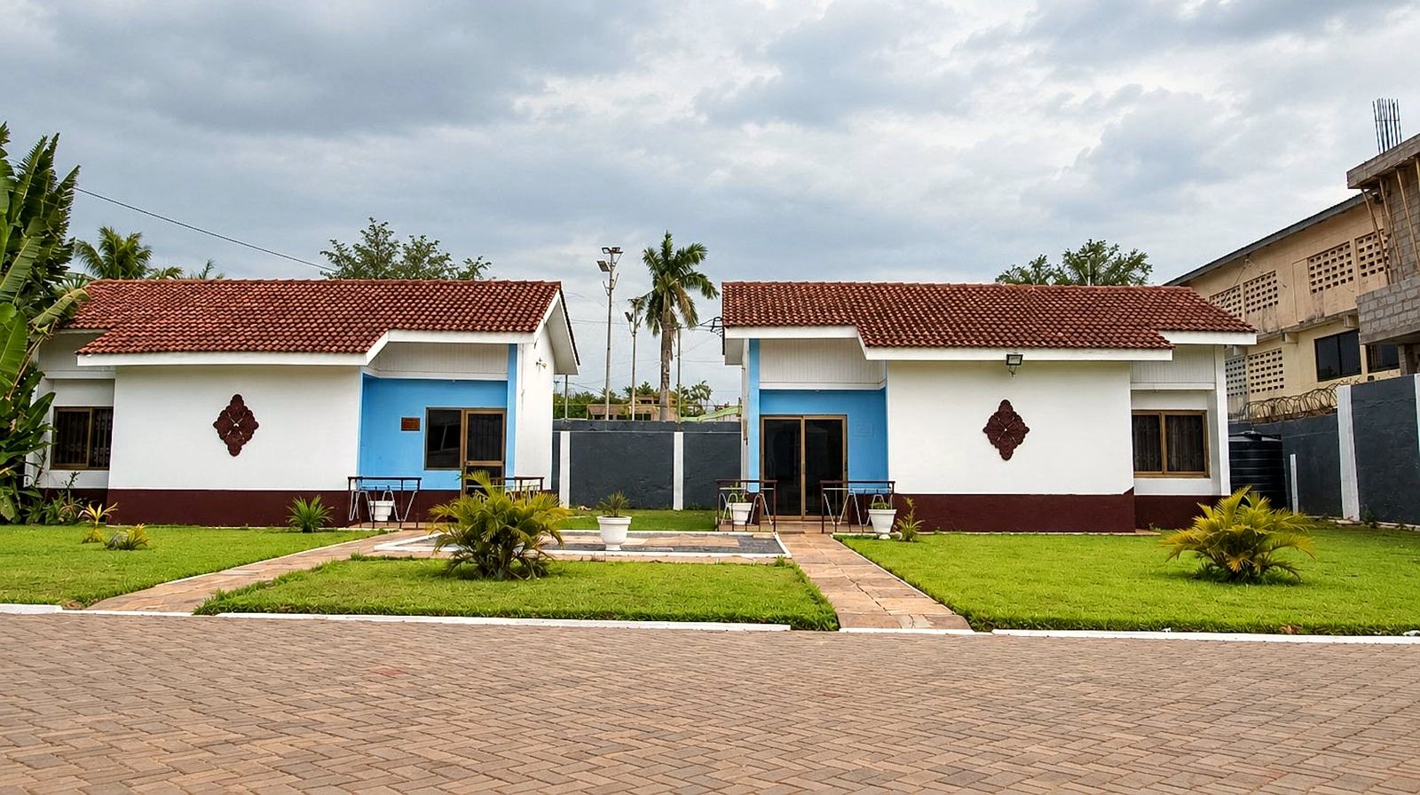 Two white and blue apartment buildings facing a lawn with palms and planting